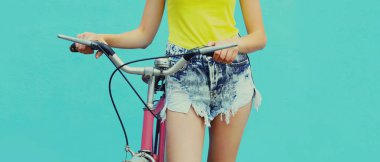 Mavi arka planda bisiklet pozu veren şortlu güzel kadın modelini kapat.