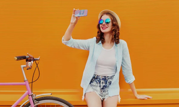 快乐的年轻微笑的女人在橙色背景下 用智能手机拍下自己的照片 — 图库照片