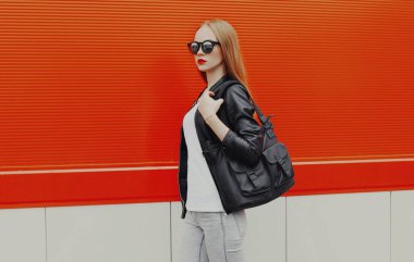 Kırmızı arka planda çantalı şık bir kadın yürüyor.