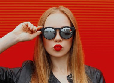 Kırmızı arka planda güneş gözlüğü takan sarışın kadının portresi.