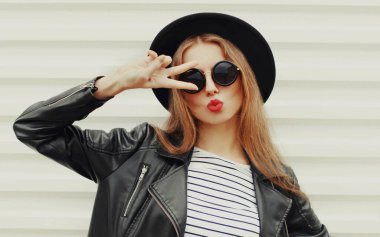 Siyah yuvarlak şapkalı, beyaz arka planda ceketli şık bir genç kadının portresi.