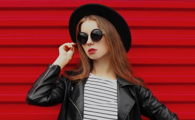 Siyah yuvarlak şapkalı, kırmızı arka planda ceketli şık bir genç kadının portresi.