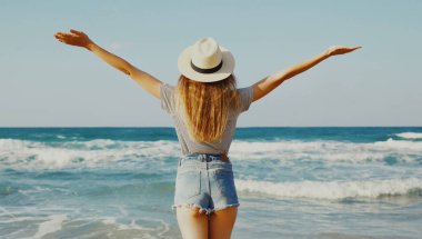 Arka planda kalan kadın yaz günü, plajda elini kaldırıyor.