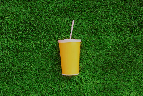 close up yellow cup of juice with straw on a green grass background, top view