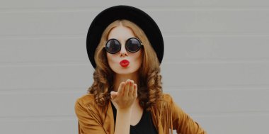 Kırmızı dudak üfleyen bir kadının portresi Gri arka planda boho tarzı tatlı bir öpücük yolluyor