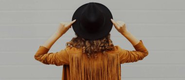 Rear view close up stylish woman wearing a black round hat, and jacket over a gray background