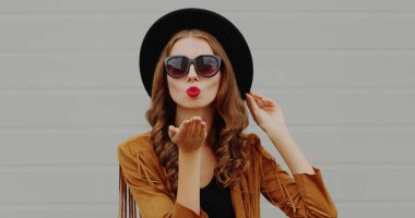 Kırmızı dudak üfleyen bir kadının portresi Gri arka planda boho tarzı tatlı bir öpücük yolluyor