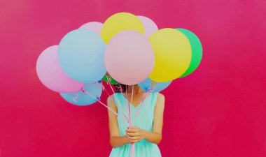 Close up woman covering her head with bunch of colorful balloons over a pink background