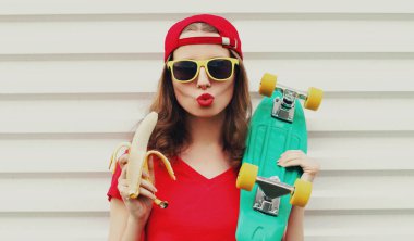 Beyaz arka planda muz ve kaykayla kırmızı dudak üfleyen kadın portresi