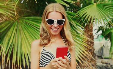 Sahilde akıllı telefonlu mutlu bir kadının yaz portresi, palmiye ağacı arka planı.