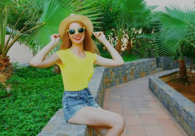 Yazın hasır şapkalı mutlu bir kadının portresi. Bir parkta, arka planda oturuyor.