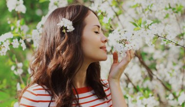 Güzel bir genç kadının portresi. Baharda çiçek açan bir bahçede. Beyaz bir çiçeğin arka planında.