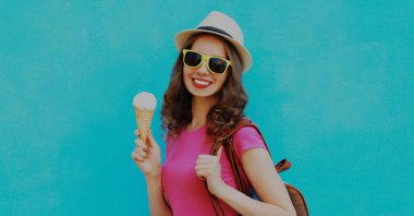 Mavi arka planda yaz hasır şapkası takan, dondurmalı mutlu genç bir kadının portresi.