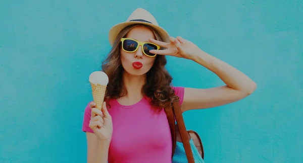 Portrait of young woman with ice cream wearing a summer straw hat on a blue background