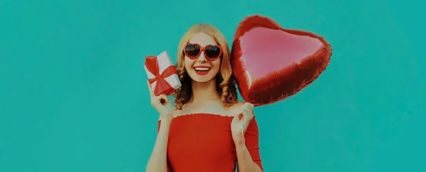 ギフトボックスと青い背景に赤いハート型の風船を持つ幸せな笑顔の女性の肖像画 — ストック写真