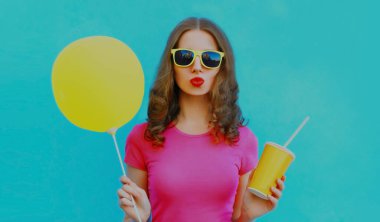 Mavi arka planda sarı balonla dudaklarını şişiren genç bir kadının yaz portresi.