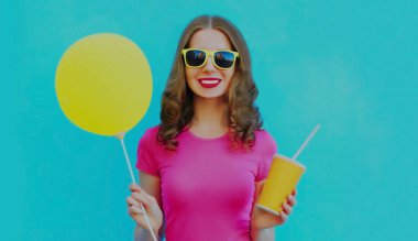 Mavi arka planda sarı balonu olan mutlu gülümseyen genç bir kadının yaz portresi