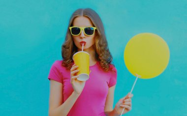 Mavi arka planda sarı balonla meyve suyu içen genç bir kadının yaz portresi