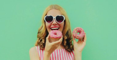 Yeşil arka planda eğlenen iki donutlu mutlu genç kadının portresi.