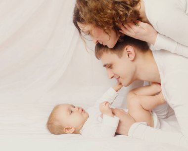 Mutlu anne ve baba evde yatakta uzanıp bebeğe bakıyor.