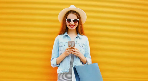 在橙色背景下 城市里拿着电话和购物袋微笑的年轻女子的画像 — 图库照片