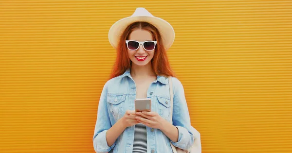 一个年轻的微笑的女人 带着夏天的草帽 带着橙色的背景 在电话里留言 — 图库照片