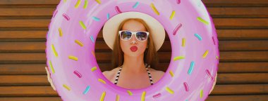 Yaz portresi, arka planda hasır şapka takan, şişme çemberle dudaklarını silen bir kadın.