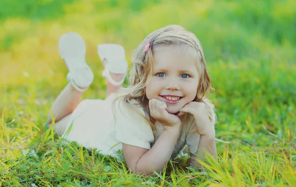 夏の公園の緑の芝生の上に横たわる幸せな笑顔の子供の肖像画 — ストック写真