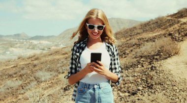 Akıllı telefonlu mutlu genç bir kadının portresi dağın tepesinde yürüyüş parkurunda, Tenerife, Kanarya Adaları, İspanya