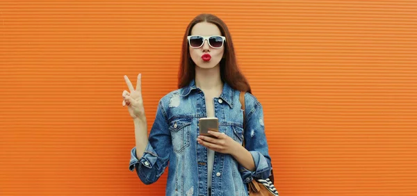 Portret Młodej Kobiety Smartfonem Dżinsowej Kurtce Pomarańczowym Tle — Zdjęcie stockowe