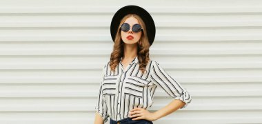 Beyaz arka planda çizgili gömlek ve siyah yuvarlak şapka giyen şık bir genç kadının portresi.