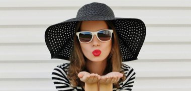 Güzel genç bir kadının portresi kırmızı dudaklarını silip siyah yuvarlak bir yaz şapkası takarak tatlı bir hava öpücüğü yolluyor.