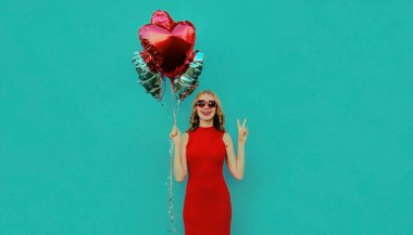 Mavi arka planda kırmızı kalp şeklinde balonları olan mutlu bir kadın.