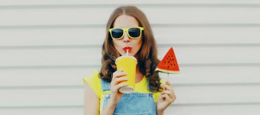 Beyaz bir arka planda dondurma şeklinde karpuz dilimiyle meyve suyu içen genç bir kadının portresi.