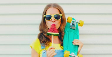 Kaykaylı genç bir kadının portresi. Beyaz bir arka planda dondurma şeklinde karpuz yiyor.