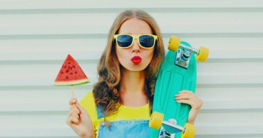 Beyaz arka planda kaykay ve dondurma şeklinde karpuz dilimi olan genç bir kadının portresi.