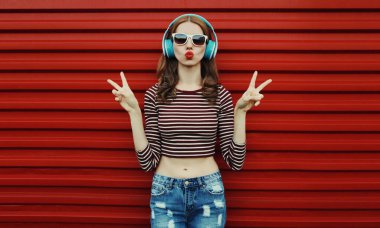 Kablosuz kulaklıklı mutlu genç bir kadının portresi kırmızı arka planda müzik dinliyor.