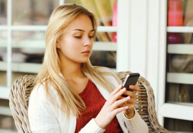 Kafedeki masada otururken telefona bakan genç bir kadının portresi.