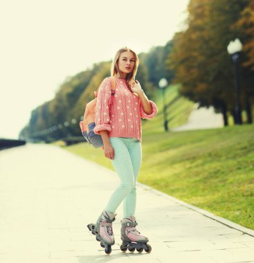 Şehir parkında sırt çantasıyla paten süren şık genç bir kadın.