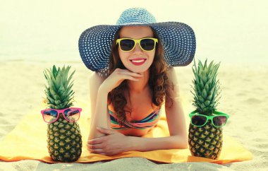 Mutlu gülümseyen genç bir kadının portresi kumsalda uzanmış komik bir ananasla hasır şapka takıyor.