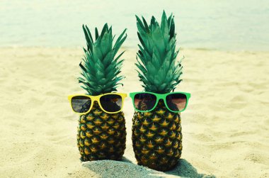 Yazın bitiminde kumsalda renkli güneş gözlüklü iki komik ananas.