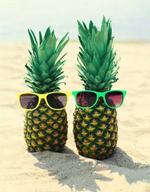 Yazın bitiminde kumsalda renkli güneş gözlüklü iki komik ananas.