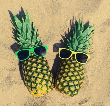 Yazın bitiminde kumsalda renkli güneş gözlüklü iki komik ananas.