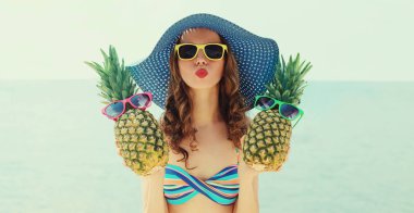 Plajda hasır şapka takmış iki komik ananasla genç bir kadının portresi.