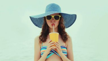 Plajda hasır şapka takıp meyve suyu içen genç bir kadının portresi.