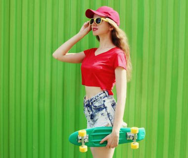 Şehirde yeşil kaykaylı, şort ve kırmızı beyzbol şapkası takan genç bir kadın.