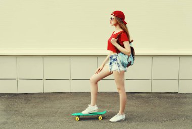 Şehirde yeşil kaykaylı, şort ve kırmızı beyzbol şapkası takan genç bir kadın.