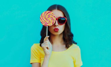 Kırmızı dudaklarını mavi arka planda lolipopla silen genç bir kadının portresi.