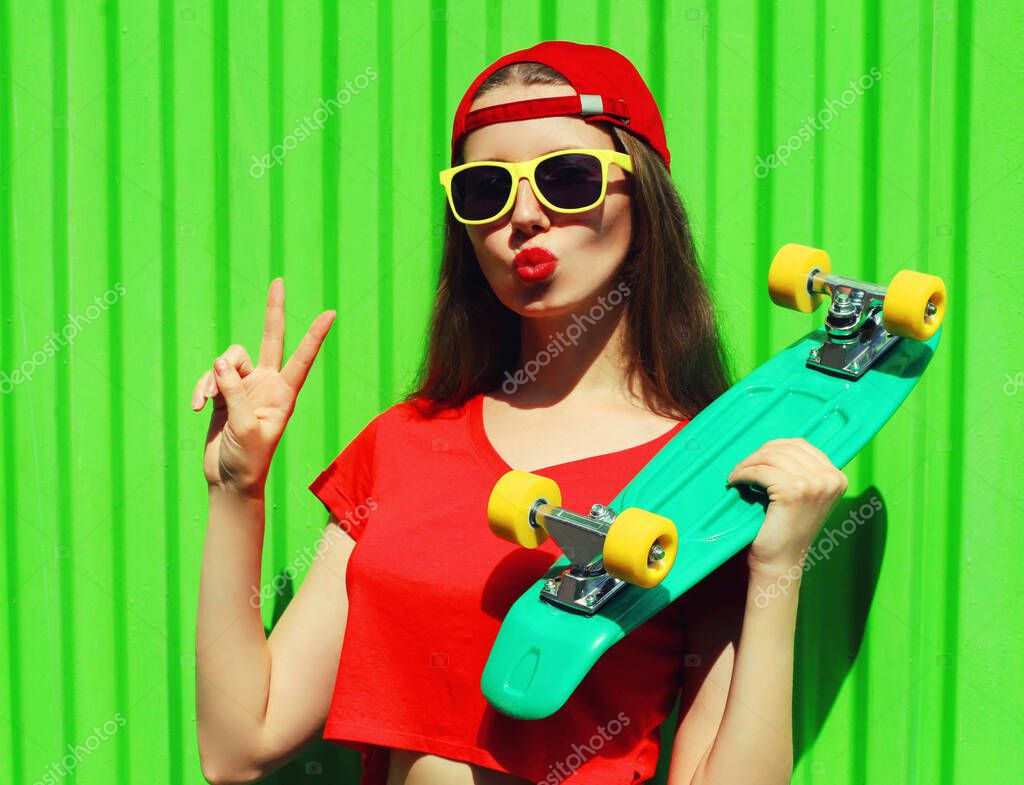 Summer portrait of cool young woman with green skateboard wearing a red baseball cap in a city