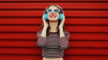 Kablosuz kulaklıklı mutlu genç bir kadının portresi kırmızı arka planda müzik dinliyor.